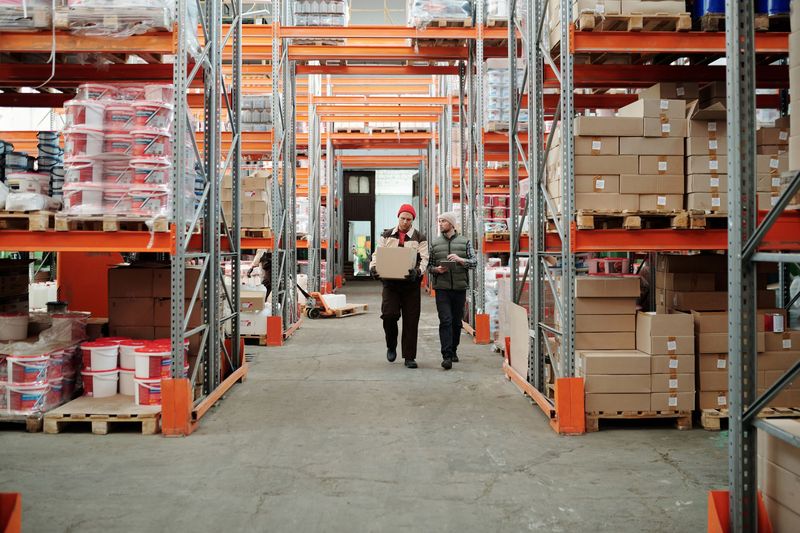 Warehouse workers moving boxes, illustrating the subcontractor network AZ-COM Maruwa will pay in JPYC stablecoin